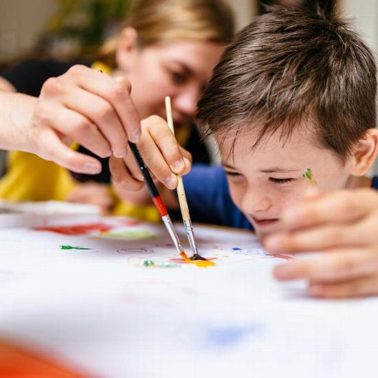 A young boy painting with help from a carer