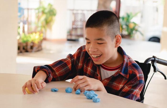 A young boy in a wheelchair playing at a table